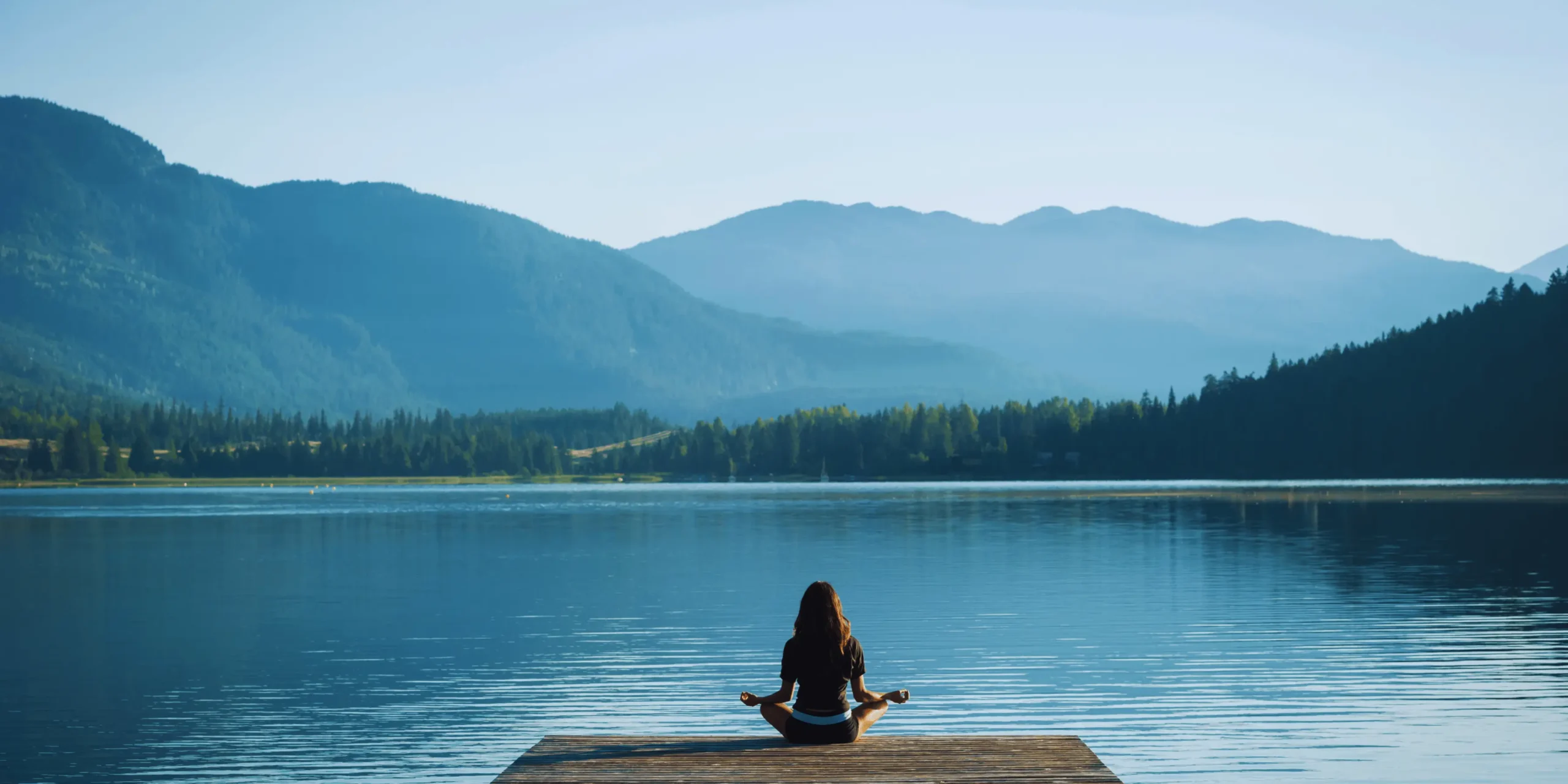 Žena medituje na molu u jezera.