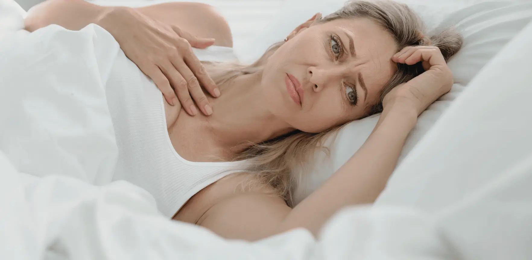 Žena leží v posteli, odpočívá, přemýšlí.